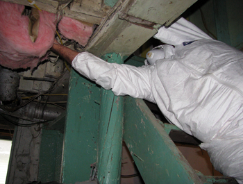 A person dressed in a white hazmat suit examines the wiring and sealing of a home