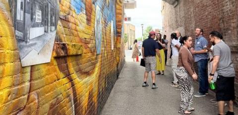 A mural with gold and blue, viewed by many onlookers, outside of a gallery run by a NeighborWorks nonprofit.